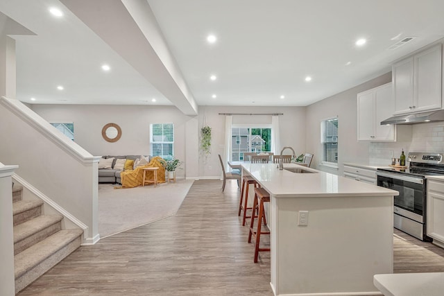 kitchen featuring stainless steel range with electric stovetop, a breakfast bar, sink, an island with sink, and white cabinetry