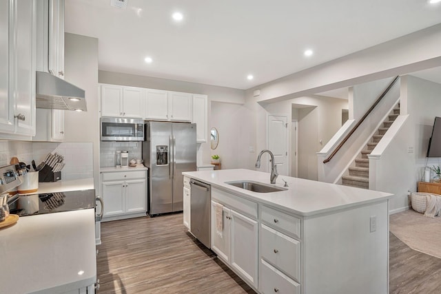 kitchen with exhaust hood, sink, an island with sink, white cabinetry, and stainless steel appliances