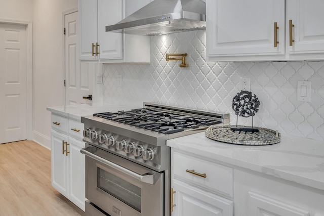 kitchen with light stone countertops, tasteful backsplash, wall chimney exhaust hood, high end stove, and light hardwood / wood-style floors