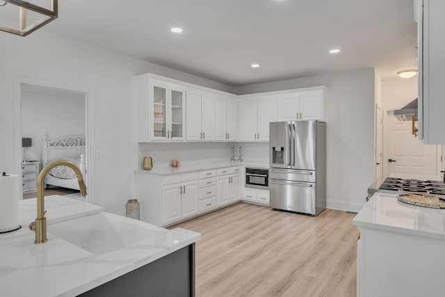 kitchen with white cabinets, ventilation hood, appliances with stainless steel finishes, tasteful backsplash, and light stone counters