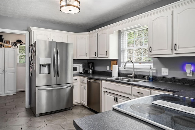 kitchen with appliances with stainless steel finishes, a textured ceiling, white cabinetry, and sink