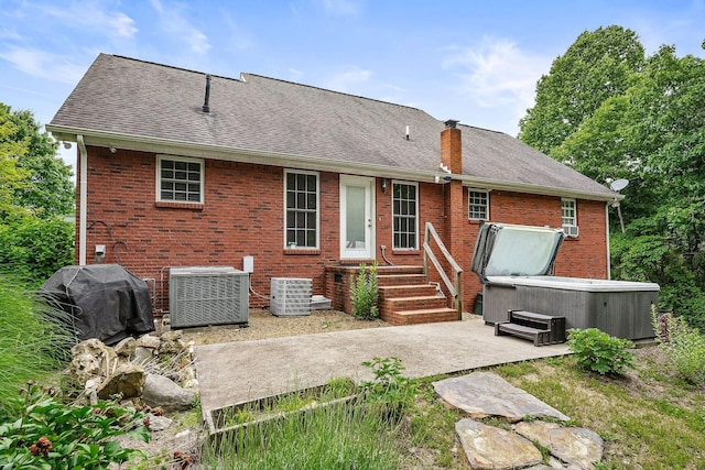 rear view of property with central AC unit, a patio area, and a hot tub