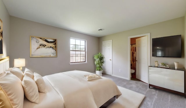 bedroom with ensuite bathroom and light colored carpet