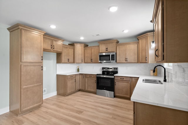 kitchen featuring light wood-type flooring, backsplash, light stone counters, stainless steel appliances, and sink