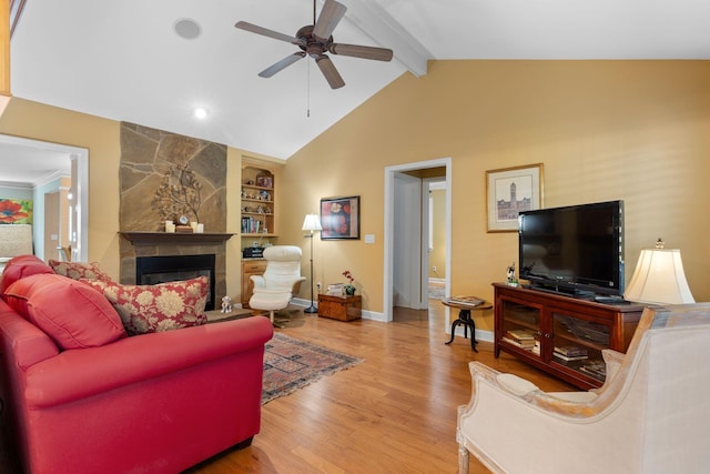 living room featuring ceiling fan, lofted ceiling with beams, built in features, hardwood / wood-style floors, and a stone fireplace