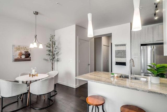 kitchen with sink, hanging light fixtures, light stone counters, kitchen peninsula, and high end fridge