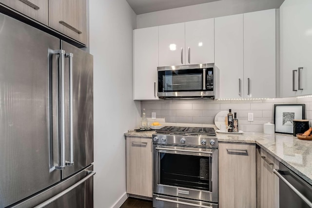 kitchen featuring dark hardwood / wood-style flooring, backsplash, light stone counters, high quality appliances, and white cabinetry