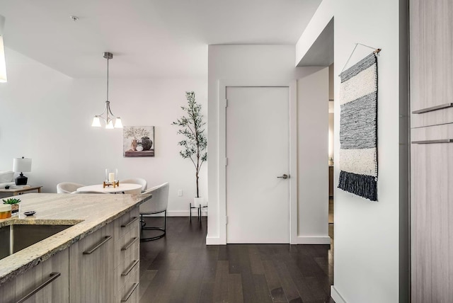 kitchen with light stone countertops, light brown cabinets, dark wood-type flooring, a notable chandelier, and decorative light fixtures