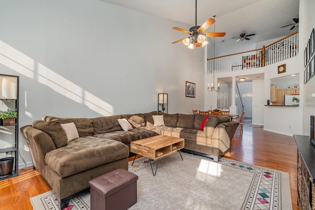 living room with high vaulted ceiling, wood-type flooring, and ceiling fan with notable chandelier