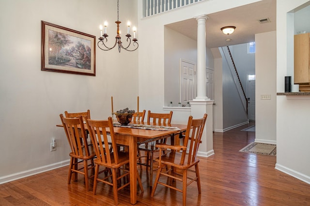 dining space with a chandelier, ornate columns, and dark wood-type flooring