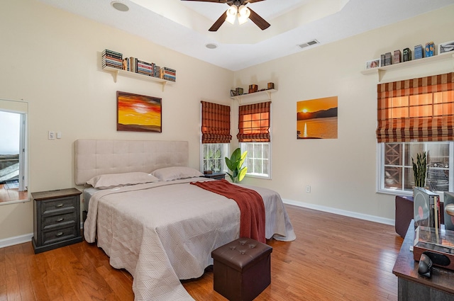 bedroom with multiple windows, hardwood / wood-style flooring, a raised ceiling, and ceiling fan