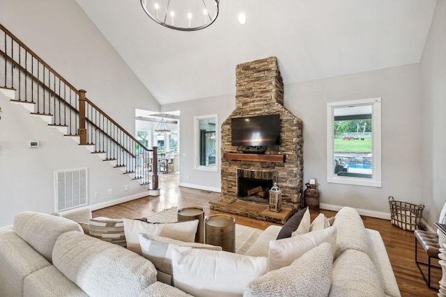 living room with hardwood / wood-style floors, an inviting chandelier, high vaulted ceiling, and a stone fireplace