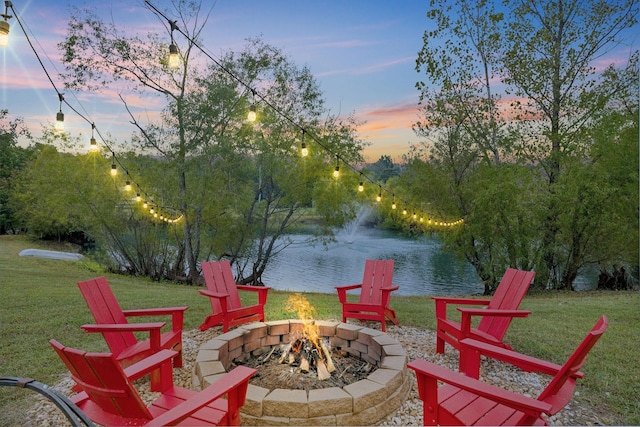 patio terrace at dusk with a water view, a fire pit, and a lawn