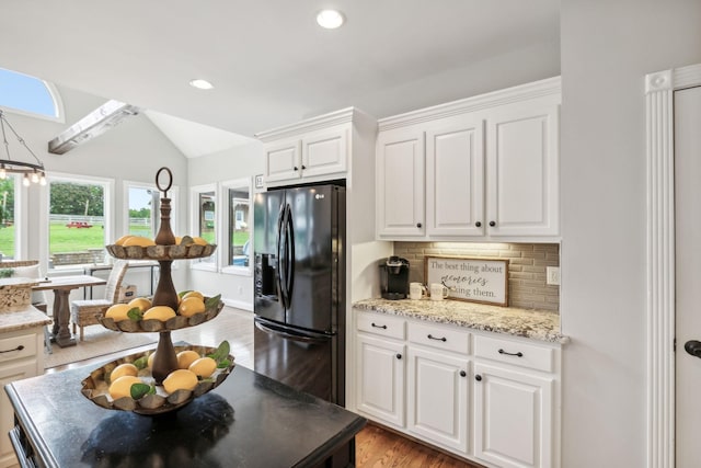 kitchen featuring white cabinetry, decorative backsplash, black fridge, and vaulted ceiling