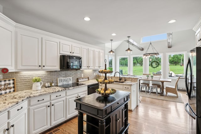 kitchen with a center island, lofted ceiling with skylight, backsplash, black appliances, and white cabinetry