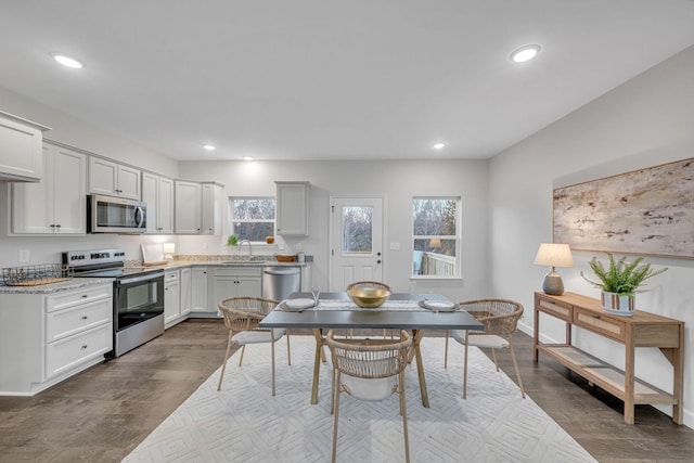 kitchen with appliances with stainless steel finishes, light stone counters, sink, dark hardwood / wood-style floors, and white cabinetry