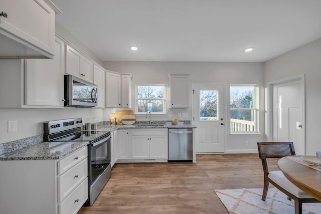 kitchen with white cabinets, sink, light wood-type flooring, light stone counters, and stainless steel appliances