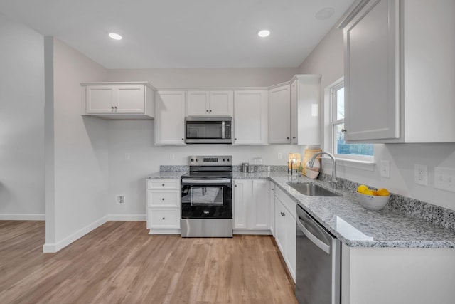 kitchen with sink, light stone countertops, light wood-type flooring, appliances with stainless steel finishes, and white cabinetry