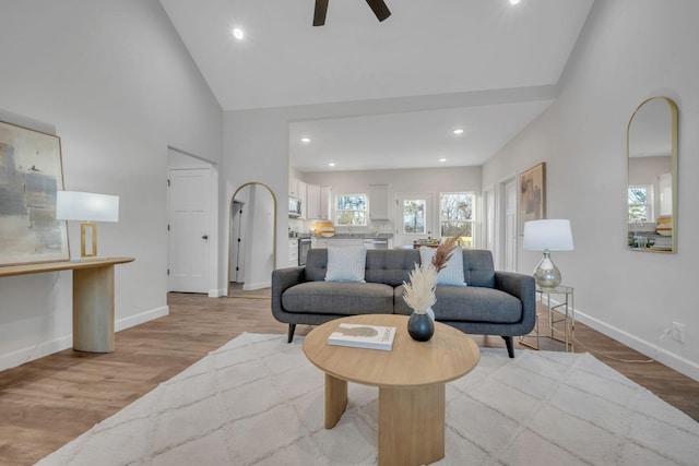 living room with ceiling fan, high vaulted ceiling, and light wood-type flooring