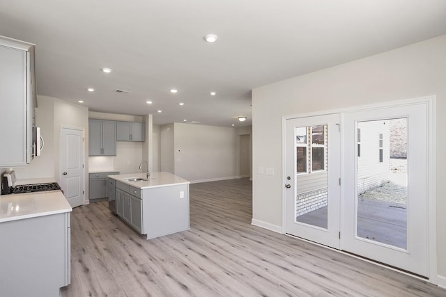 kitchen featuring sink, light hardwood / wood-style flooring, stove, gray cabinets, and a kitchen island with sink