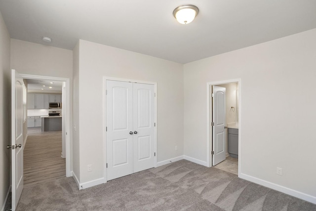 unfurnished bedroom with light colored carpet, ensuite bath, and a closet