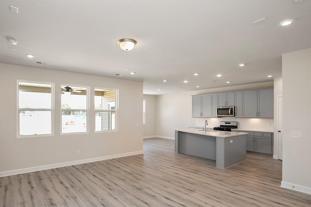 kitchen with light wood-type flooring, gray cabinetry, stainless steel appliances, sink, and a center island with sink