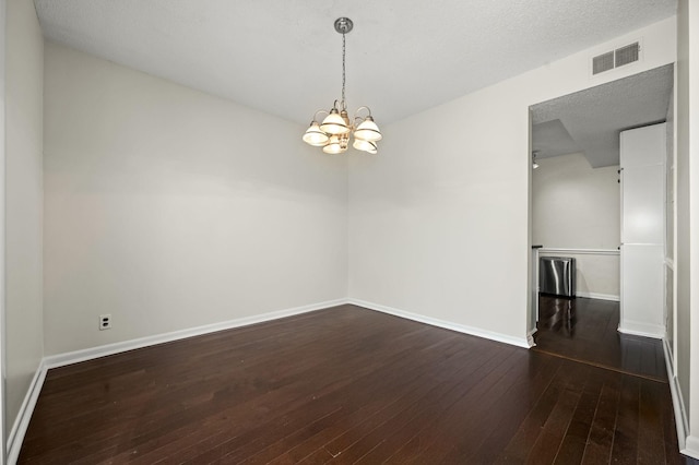 empty room with dark hardwood / wood-style floors, a textured ceiling, and an inviting chandelier