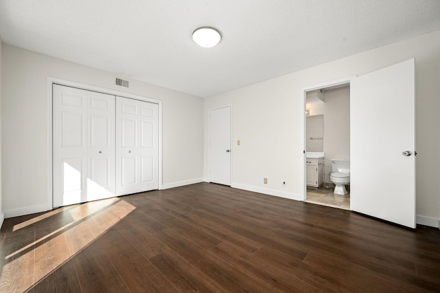 unfurnished bedroom featuring dark hardwood / wood-style flooring, a textured ceiling, ensuite bath, and a closet