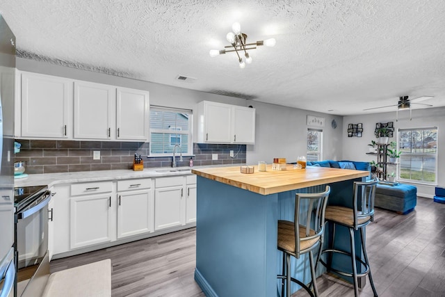 kitchen featuring sink, white cabinets, range, a kitchen island, and butcher block counters