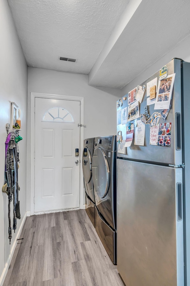 laundry room featuring light hardwood / wood-style floors, washing machine and dryer, and a textured ceiling