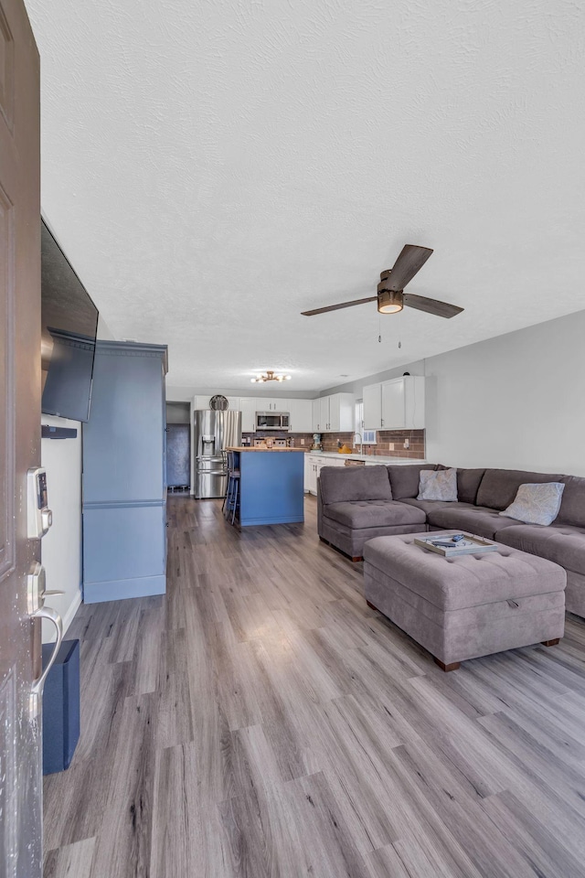 living room with ceiling fan, light hardwood / wood-style floors, and a textured ceiling