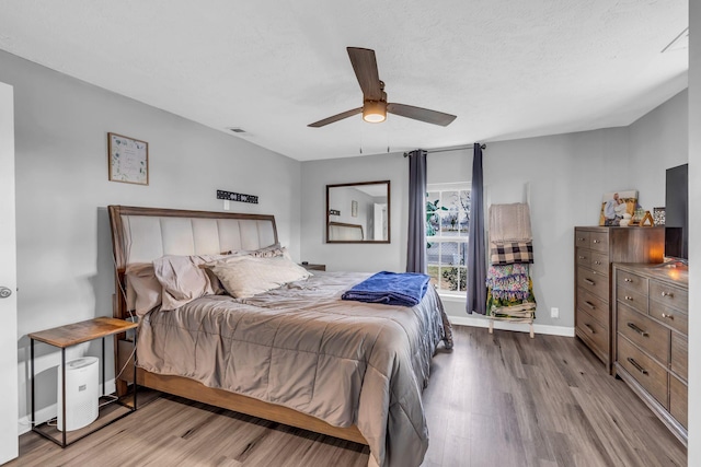 bedroom with a textured ceiling, light hardwood / wood-style flooring, and ceiling fan