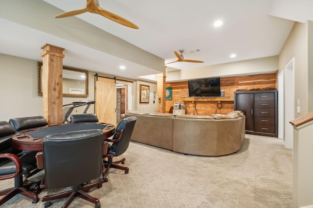 carpeted living room with a barn door, decorative columns, ceiling fan, and wooden walls