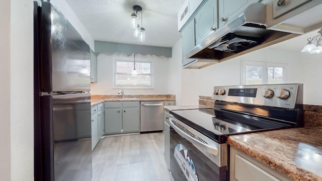 kitchen with sink, hanging light fixtures, light hardwood / wood-style flooring, a textured ceiling, and appliances with stainless steel finishes