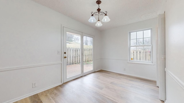 unfurnished dining area with light wood-type flooring, a textured ceiling, and a notable chandelier