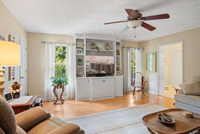 living room with ceiling fan, a textured ceiling, and light hardwood / wood-style flooring