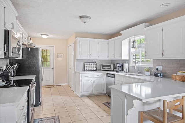 kitchen featuring kitchen peninsula, stainless steel appliances, sink, light tile patterned floors, and white cabinets