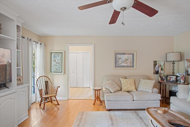 living room featuring ceiling fan, a textured ceiling, and light wood-type flooring