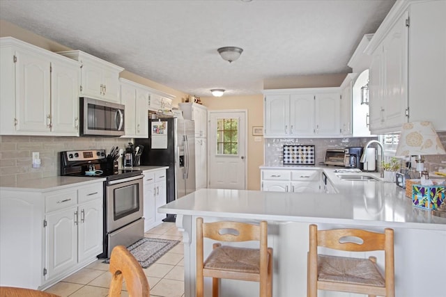 kitchen with white cabinetry, sink, kitchen peninsula, light tile patterned floors, and appliances with stainless steel finishes