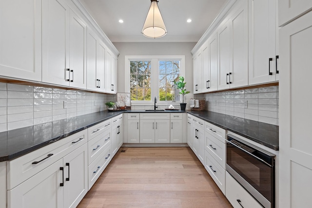 kitchen featuring backsplash, white cabinets, pendant lighting, and light wood-type flooring