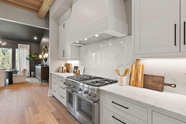 kitchen with white cabinetry, light stone counters, beamed ceiling, premium range hood, and double oven range