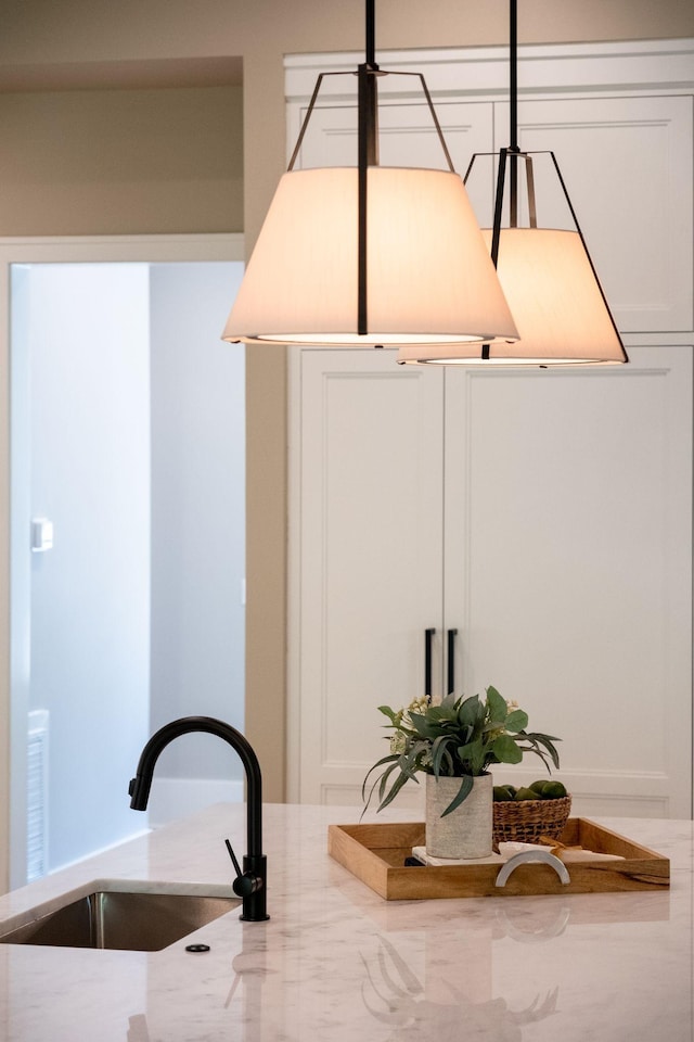 room details featuring white cabinets, light stone counters, and sink