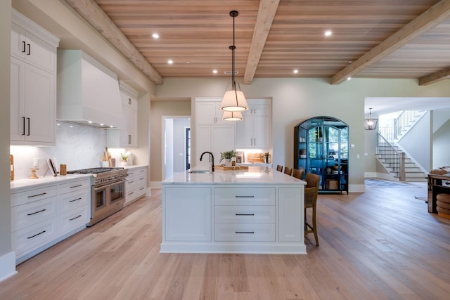 kitchen with wall chimney exhaust hood, a spacious island, range with two ovens, wooden ceiling, and white cabinetry