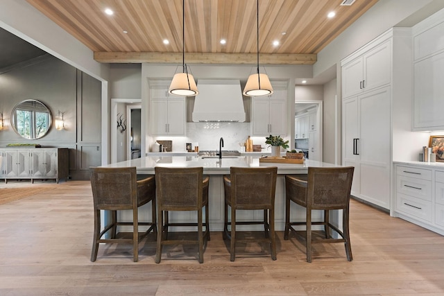 kitchen with a kitchen bar, custom range hood, beam ceiling, decorative light fixtures, and a large island