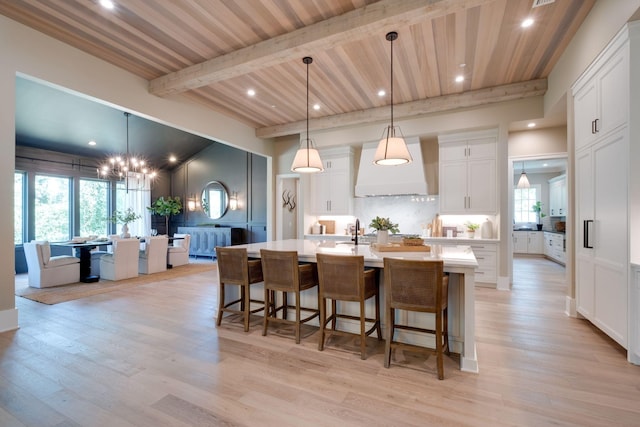 kitchen featuring pendant lighting, premium range hood, beamed ceiling, a large island, and white cabinetry