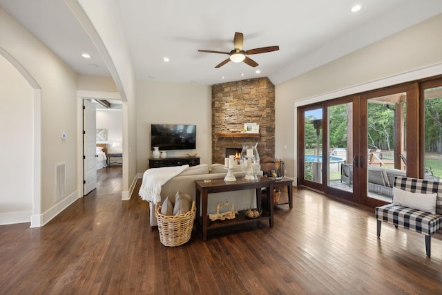 living room with french doors, a stone fireplace, vaulted ceiling, ceiling fan, and dark hardwood / wood-style flooring