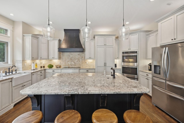 kitchen featuring appliances with stainless steel finishes, custom exhaust hood, a breakfast bar, sink, and a center island with sink