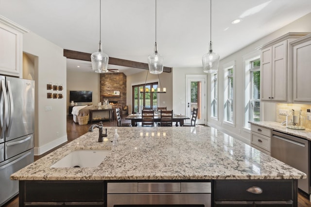 kitchen featuring a center island with sink, decorative light fixtures, light stone counters, and appliances with stainless steel finishes