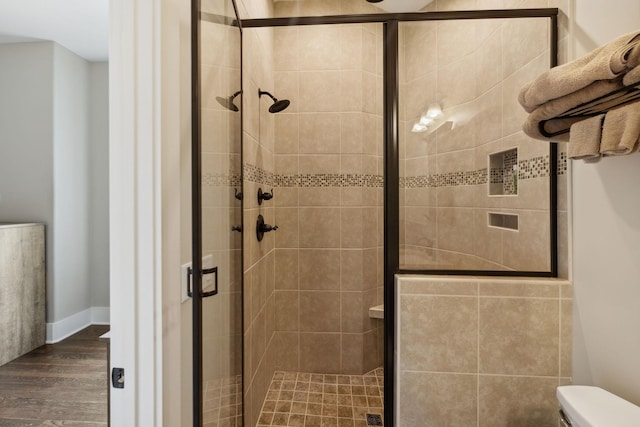 bathroom with toilet, an enclosed shower, and wood-type flooring