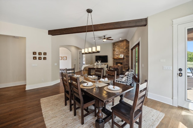 dining area with hardwood / wood-style floors, ceiling fan, beam ceiling, and a stone fireplace